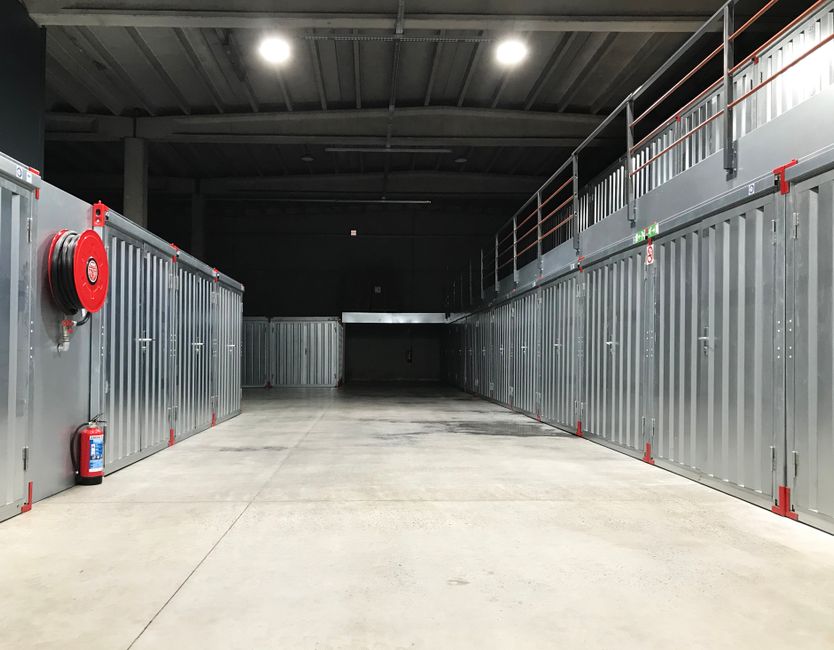 Wide indoor self storage aisle with steel unit doors on both sides and a mezzanine level above