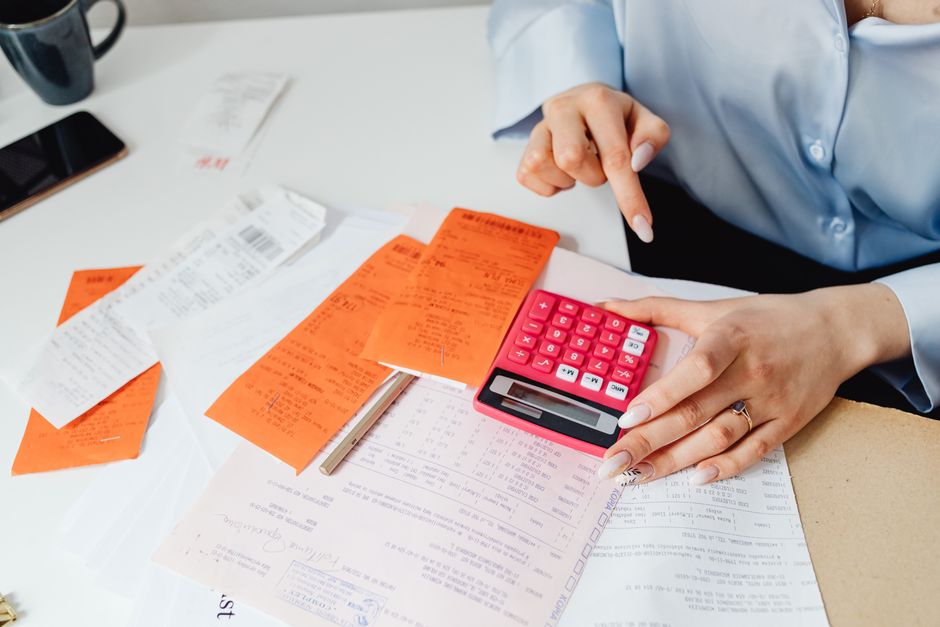 Person adding up paper receipts with a calculator at a desk