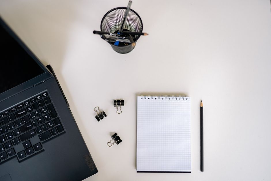 Blank notepad, pencil and laptop on a white desk