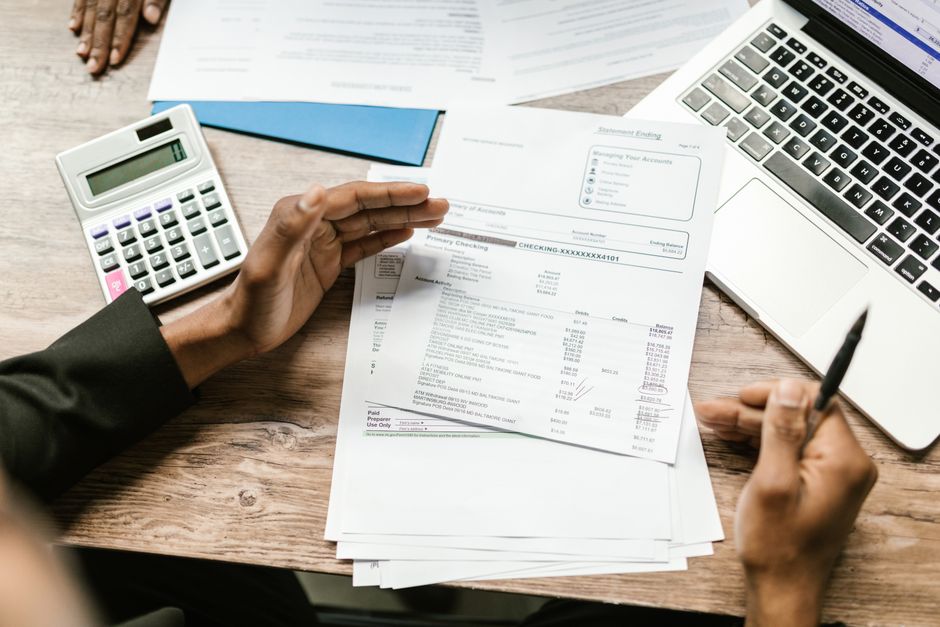 Hands holding a printed statement beside a calculator and a laptop