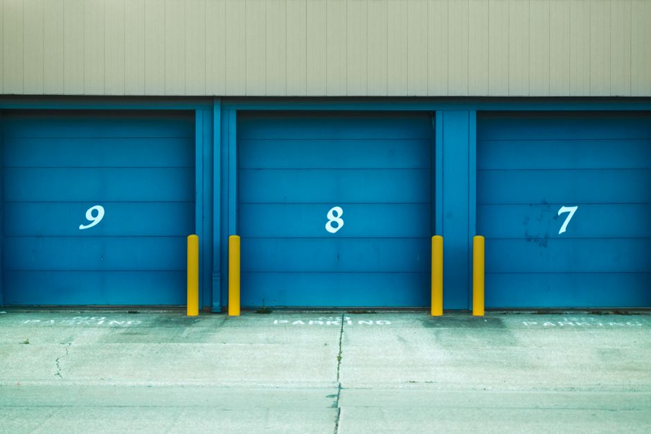 Three numbered blue roll-up doors with yellow bollards outside a storage building